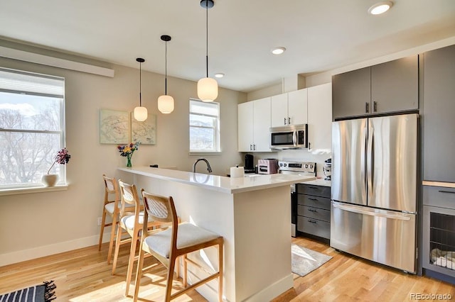 kitchen featuring a breakfast bar area, hanging light fixtures, stainless steel appliances, light hardwood / wood-style floors, and white cabinets