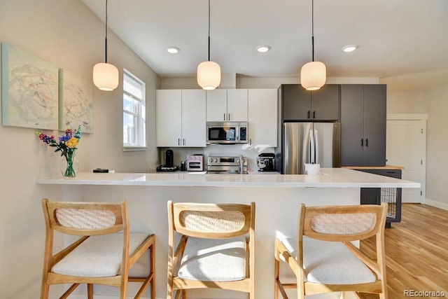 kitchen with stainless steel appliances, white cabinetry, and decorative light fixtures