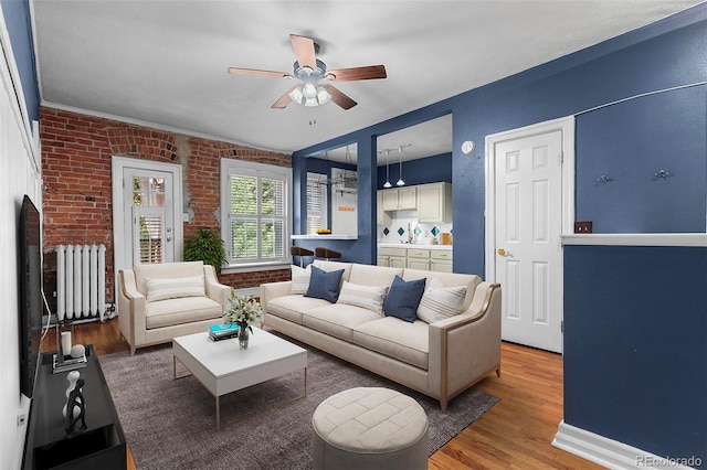 living room with brick wall, hardwood / wood-style floors, and ceiling fan