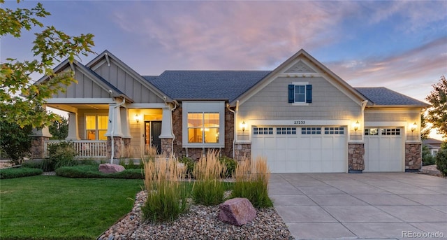 craftsman-style house featuring covered porch, stone siding, concrete driveway, board and batten siding, and a front yard