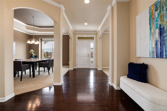 entryway with a notable chandelier, dark wood-type flooring, ornamental molding, and baseboards