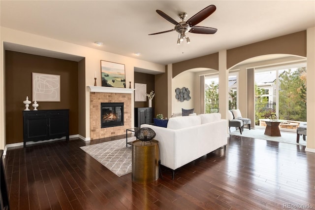 living area with a ceiling fan, a glass covered fireplace, dark wood finished floors, and baseboards