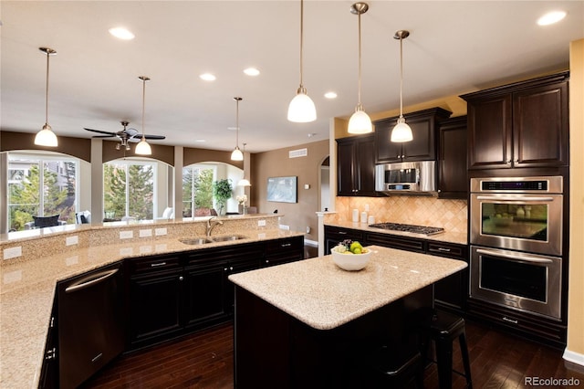 kitchen featuring arched walkways, a kitchen island, a sink, hanging light fixtures, and appliances with stainless steel finishes