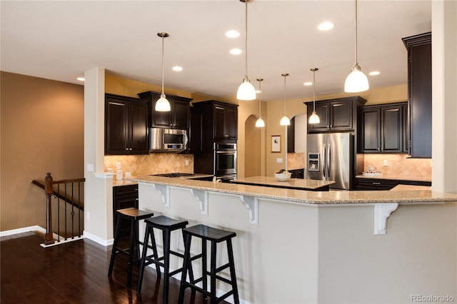 kitchen with light stone counters, a breakfast bar, pendant lighting, arched walkways, and appliances with stainless steel finishes