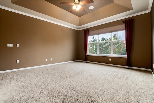 carpeted spare room featuring a ceiling fan, a tray ceiling, crown molding, and baseboards