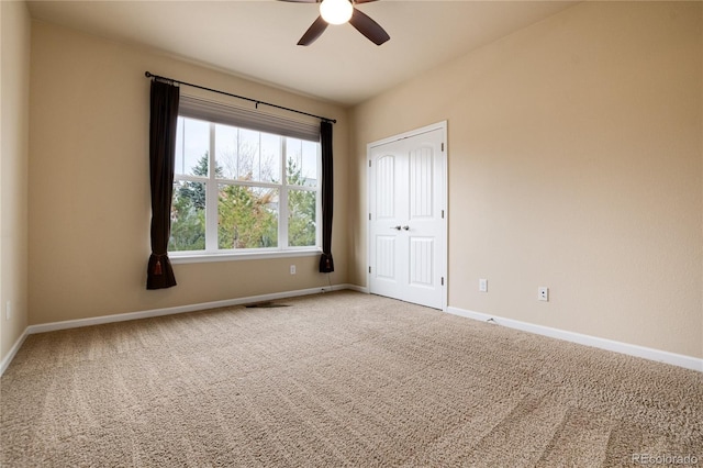 carpeted spare room with visible vents, baseboards, and a ceiling fan