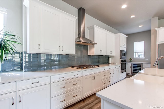 9571 Yucca Ct, Arvada, CO 80007 - kitchen featuring wall chimney exhaust hood, stainless steel appliances, wine cooler, white cabinetry, and light countertops