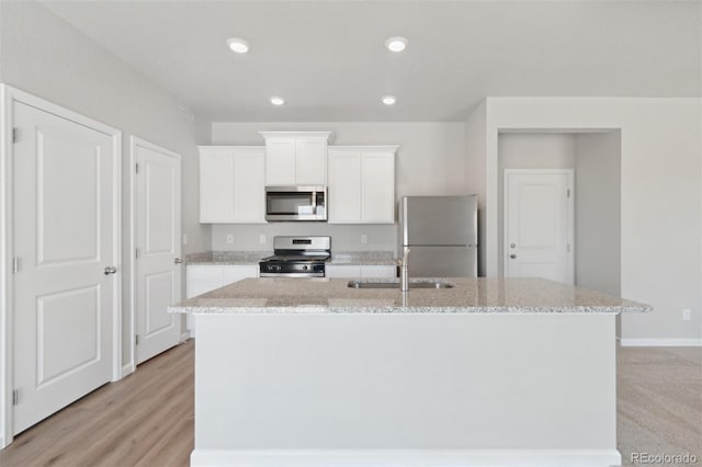 kitchen with light stone counters, a center island with sink, a sink, appliances with stainless steel finishes, and white cabinetry