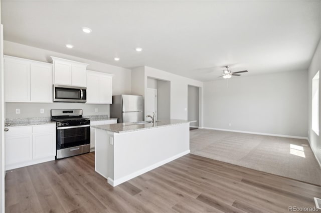 kitchen with light wood-type flooring, an island with sink, a ceiling fan, white cabinetry, and stainless steel appliances