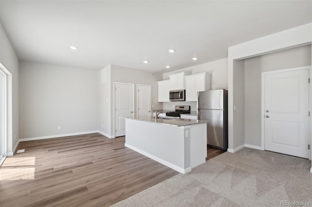 kitchen with light carpet, a kitchen island with sink, white cabinetry, appliances with stainless steel finishes, and light stone counters