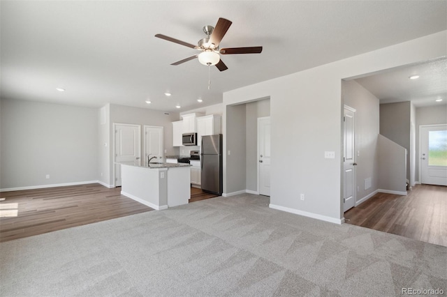 kitchen featuring ceiling fan, white cabinets, dark carpet, stainless steel appliances, and an island with sink