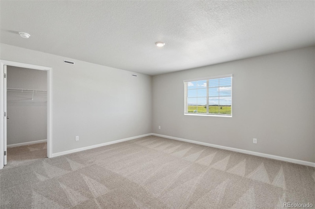 unfurnished bedroom with light colored carpet, a textured ceiling, a closet, and a walk in closet