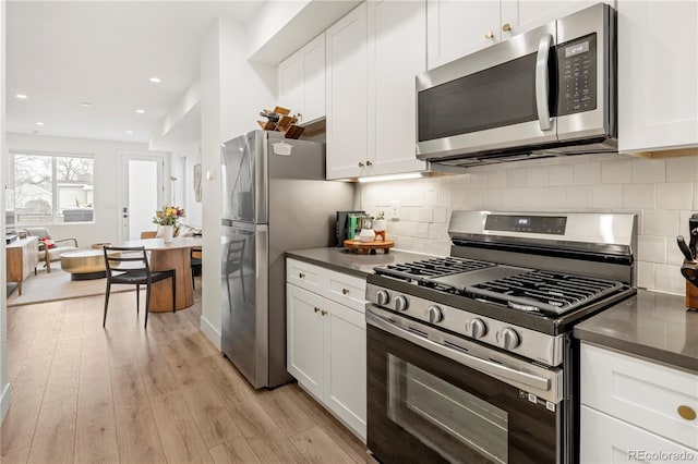 2012 W 46th Ave, Denver, CO 80211 - kitchen featuring stainless steel appliances, dark countertops, light wood-style flooring, white cabinetry, and tasteful backsplash