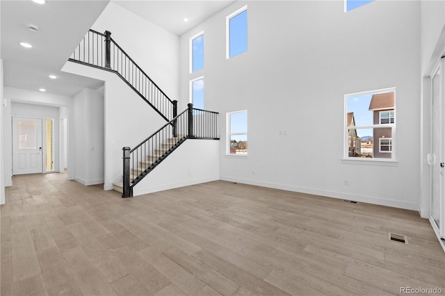 unfurnished living room featuring stairway, light wood-type flooring, a wealth of natural light, and baseboards