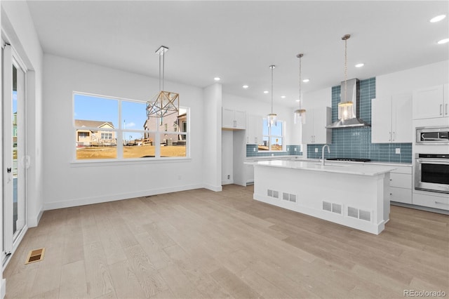 kitchen featuring light wood-style floors, light countertops, appliances with stainless steel finishes, backsplash, and wall chimney exhaust hood