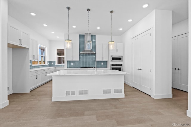 kitchen with light wood-style flooring, stainless steel appliances, white cabinets, light countertops, and wall chimney exhaust hood