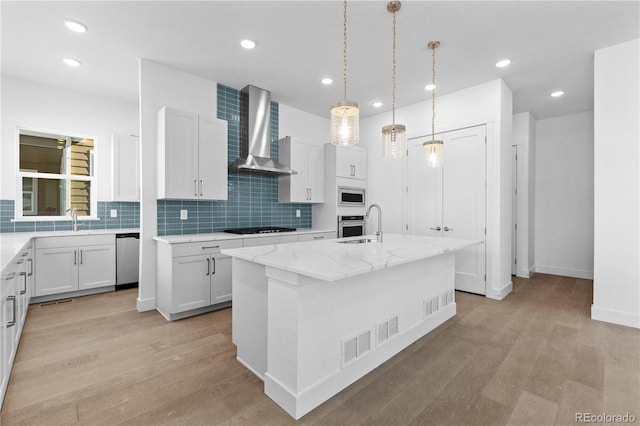 kitchen featuring stainless steel appliances, light wood-style flooring, wall chimney range hood, and light stone counters