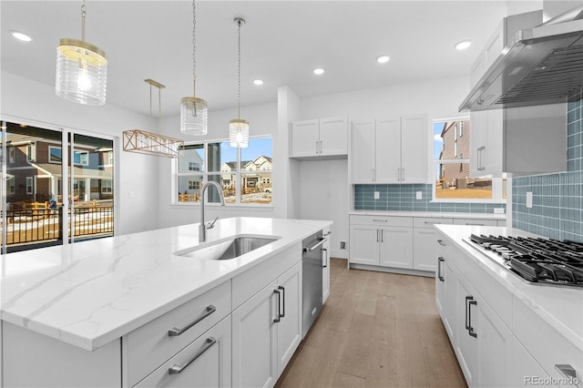 kitchen with decorative backsplash, stainless steel appliances, light wood-type flooring, wall chimney range hood, and a sink