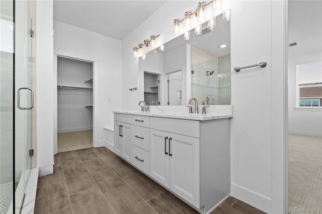 bathroom with double vanity, a stall shower, a walk in closet, and a sink