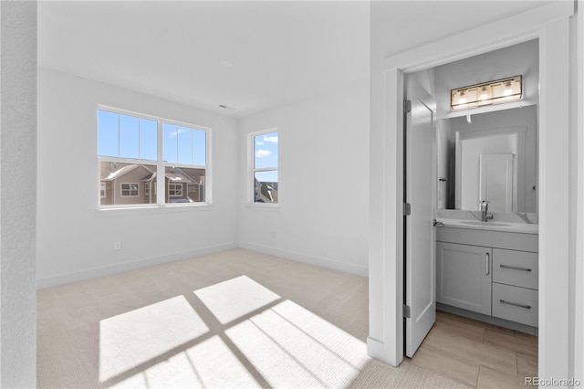 unfurnished bedroom featuring light carpet, a sink, and baseboards