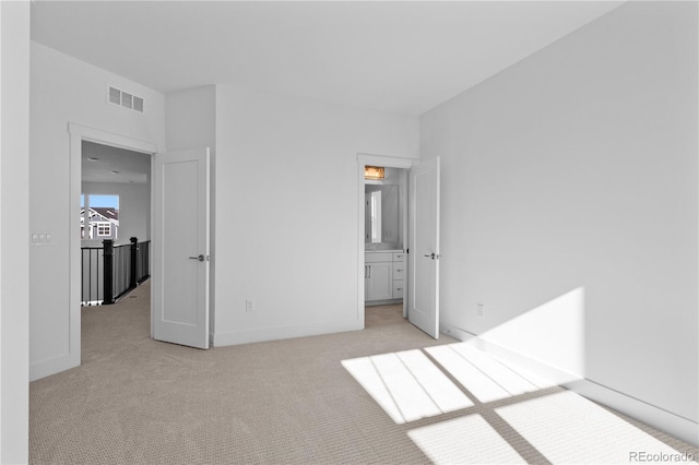 unfurnished bedroom featuring baseboards, ensuite bathroom, visible vents, and light colored carpet