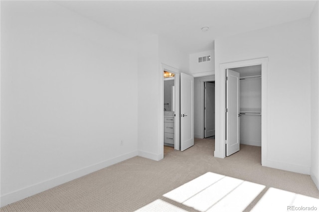 unfurnished bedroom featuring a walk in closet, visible vents, light carpet, and baseboards