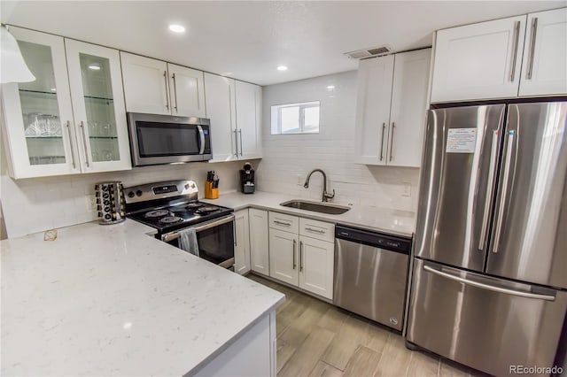 kitchen featuring stainless steel appliances, white cabinetry, sink, and light stone counters