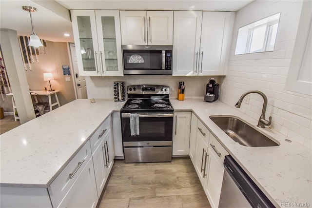 kitchen with decorative light fixtures, white cabinetry, sink, light stone counters, and stainless steel appliances