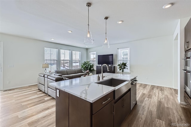 kitchen featuring dark brown cabinetry, a sink, light wood-style floors, open floor plan, and light stone countertops