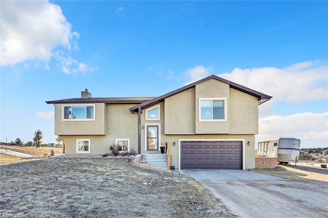 bi-level home with driveway, a chimney, an attached garage, and stucco siding