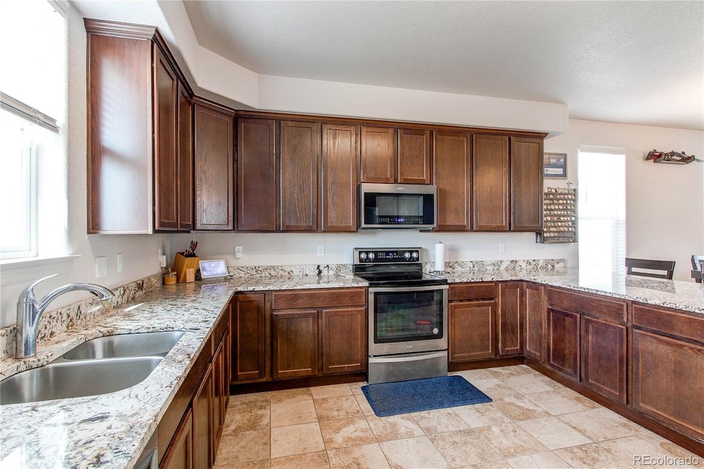 kitchen with stainless steel appliances, light stone countertops, and sink