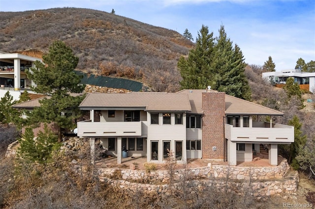 rear view of house featuring a mountain view, a balcony, and a patio