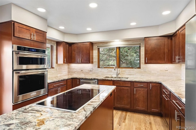 kitchen with decorative backsplash, appliances with stainless steel finishes, light wood-type flooring, light stone counters, and sink