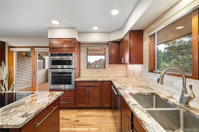 kitchen with appliances with stainless steel finishes, light wood-type flooring, backsplash, light stone counters, and sink