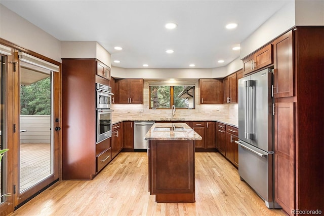 kitchen with light stone countertops, sink, stainless steel appliances, a kitchen island, and light wood-type flooring