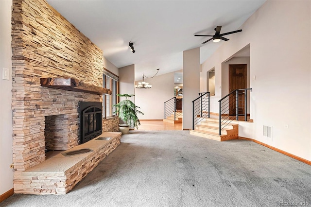 unfurnished living room featuring ceiling fan with notable chandelier, vaulted ceiling, a stone fireplace, and carpet flooring