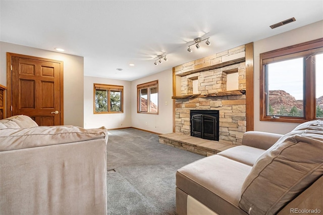 carpeted living room featuring rail lighting and a stone fireplace