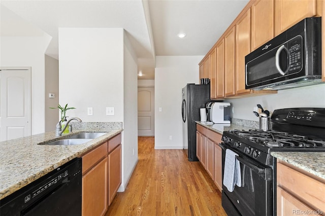 kitchen with light stone counters, black appliances, sink, and light wood-type flooring