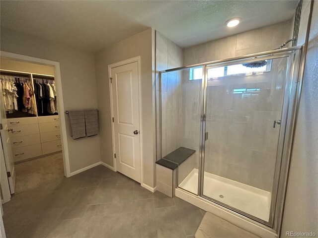 12901 Crane River Dr, Longmont, CO 80504 - bathroom featuring a shower stall, a walk in closet, baseboards, and tile patterned flooring