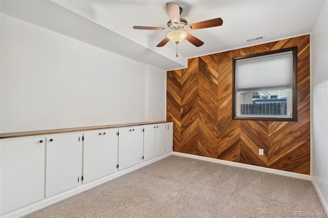 carpeted spare room with ceiling fan and wood walls