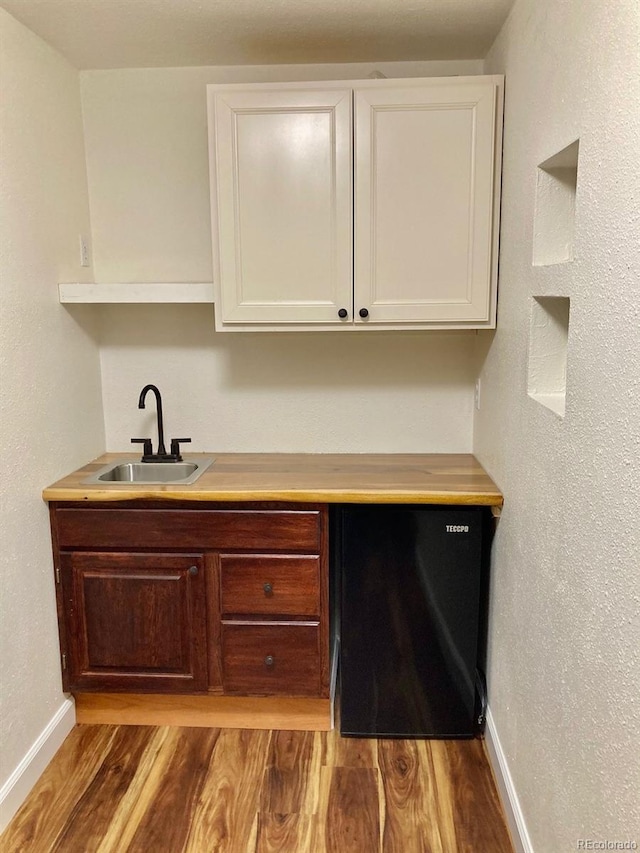 bar featuring black refrigerator, light hardwood / wood-style floors, sink, and white cabinetry