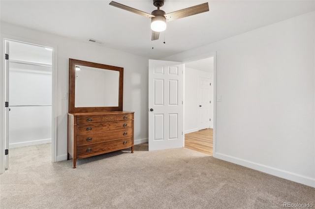 unfurnished bedroom with a walk in closet, ceiling fan, a closet, and light colored carpet