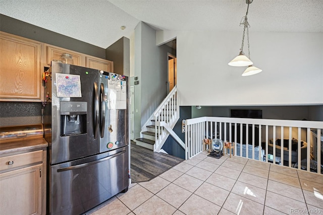 kitchen featuring light brown cabinets, lofted ceiling, hanging light fixtures, stainless steel refrigerator with ice dispenser, and tile countertops