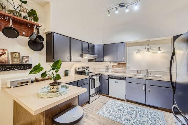 kitchen with appliances with stainless steel finishes, track lighting, sink, decorative light fixtures, and light wood-type flooring