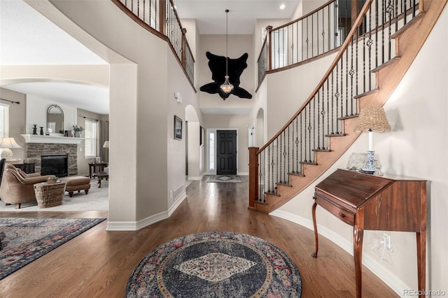 foyer entrance with a stone fireplace, stairway, wood finished floors, and baseboards