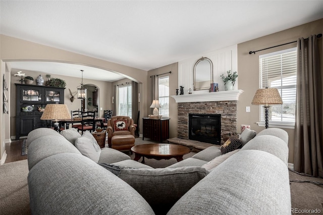 living area featuring arched walkways, a chandelier, and a stone fireplace