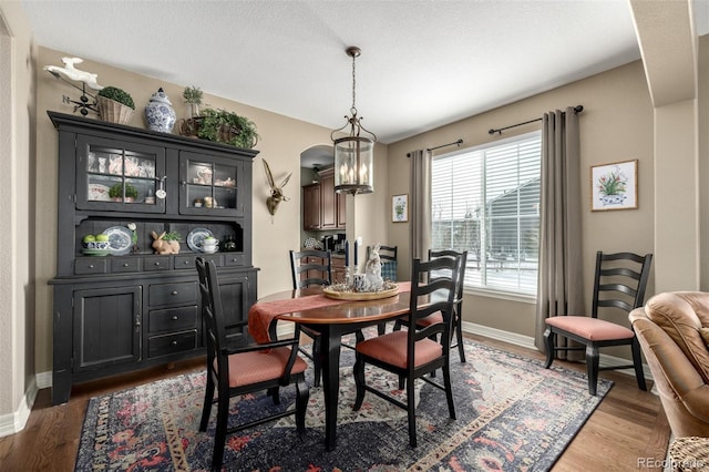 dining area with a chandelier, arched walkways, baseboards, and light wood finished floors