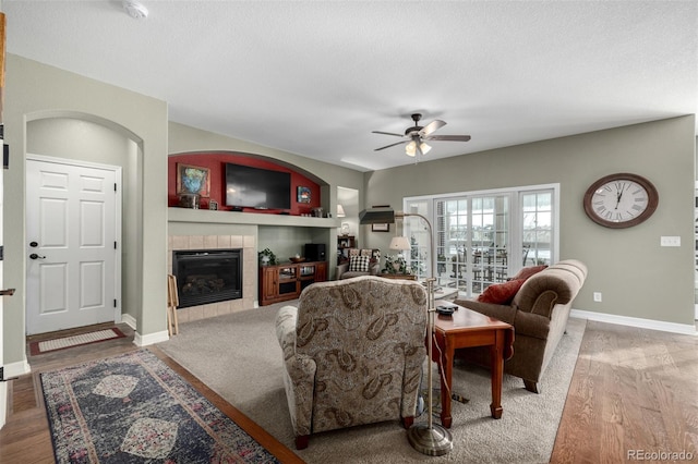 living room featuring ceiling fan, baseboards, wood finished floors, and a tile fireplace