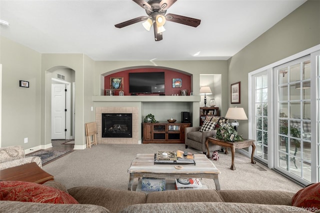 living room featuring baseboards, visible vents, a ceiling fan, a tiled fireplace, and carpet flooring