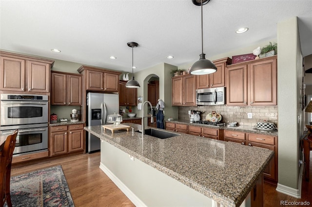 kitchen featuring appliances with stainless steel finishes, brown cabinets, a sink, and wood finished floors